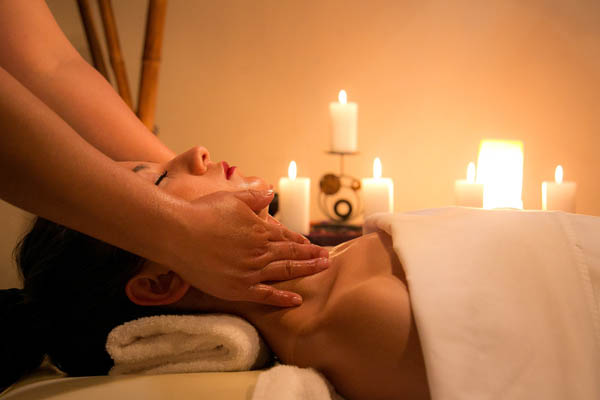 Woman on table laying on back getting a massage with candles in the background 600