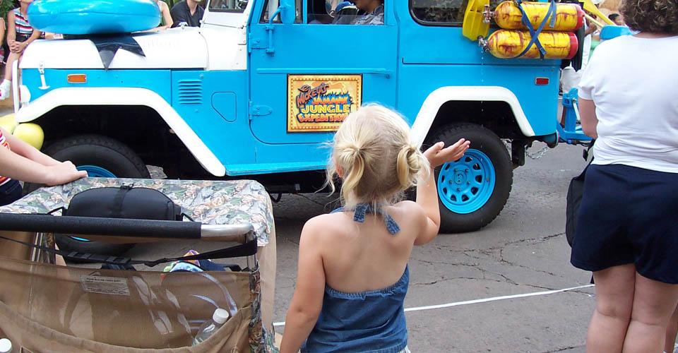 Child in the Disney World parade line waving to the cars passing by