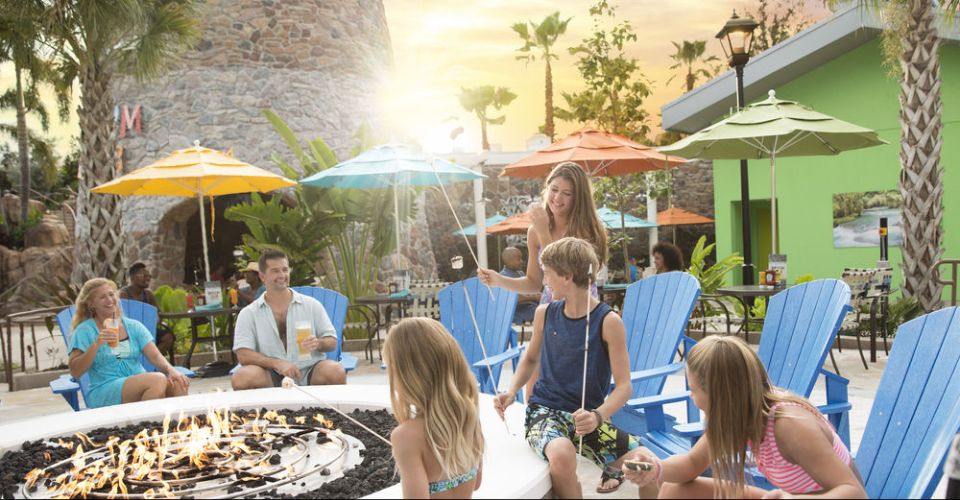 Family enjoying time together roasting marshmallows around the large firepit at the Loews Sapphire Falls Resort Huge Outdoor Pool in Orlando