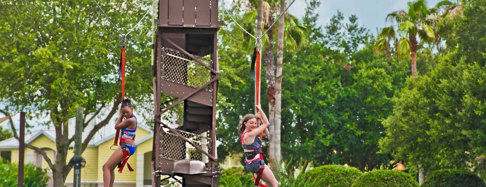 Two Zip lines from a single tower with riders swinging above one of the lakes on the Summer Bay Resort Orlando